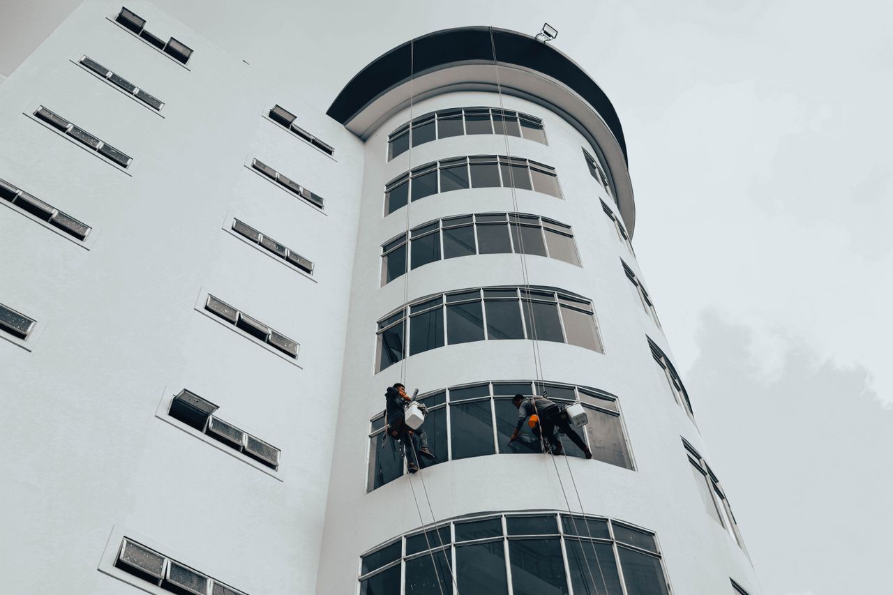 Workers cleaning white curved commercial building using rope access