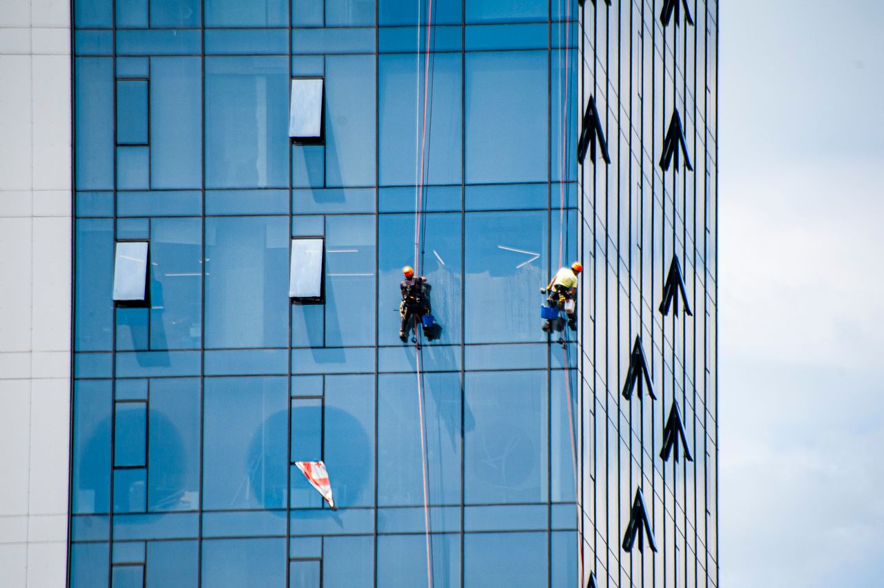 Facade cleaning workers with safety helmets on blue glass building using rope access