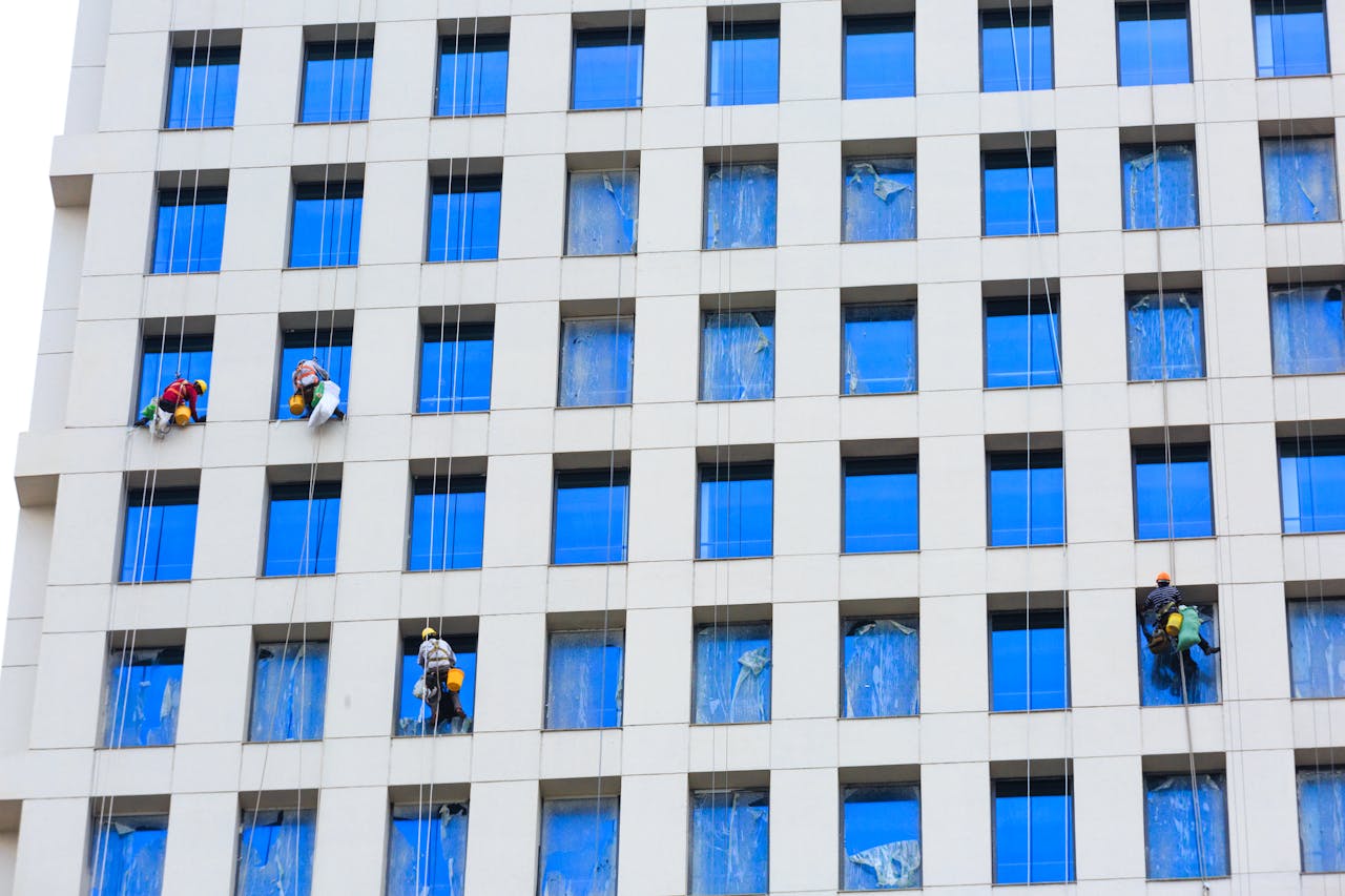 Facade cleaning workers on a large white building with blue windows in polluted Indian city