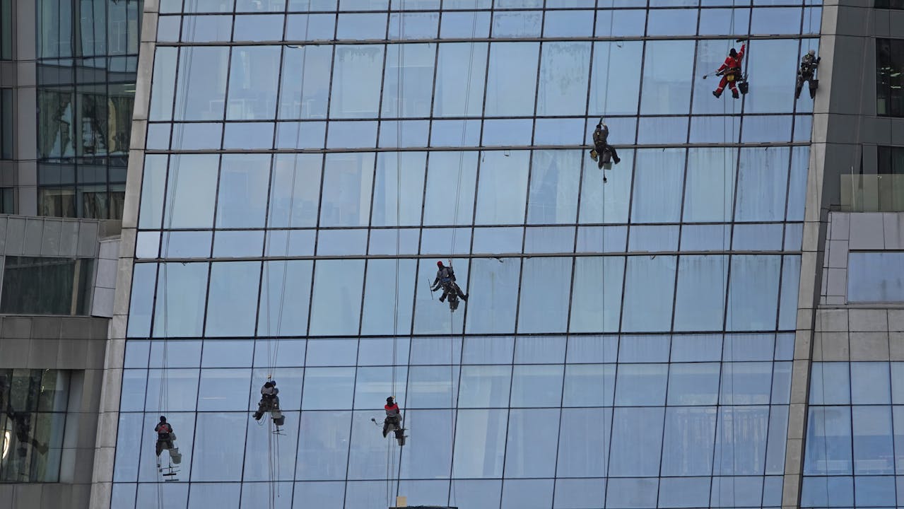 Multiple workers on ropes cleaning a large glass building facade