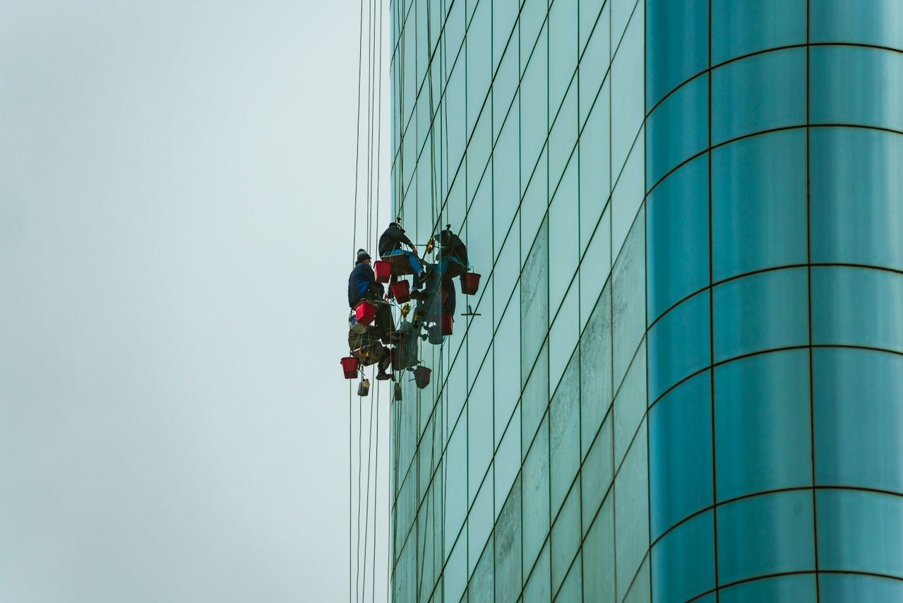 Professional facade cleaning workers on rope access cleaning commercial building glass facade